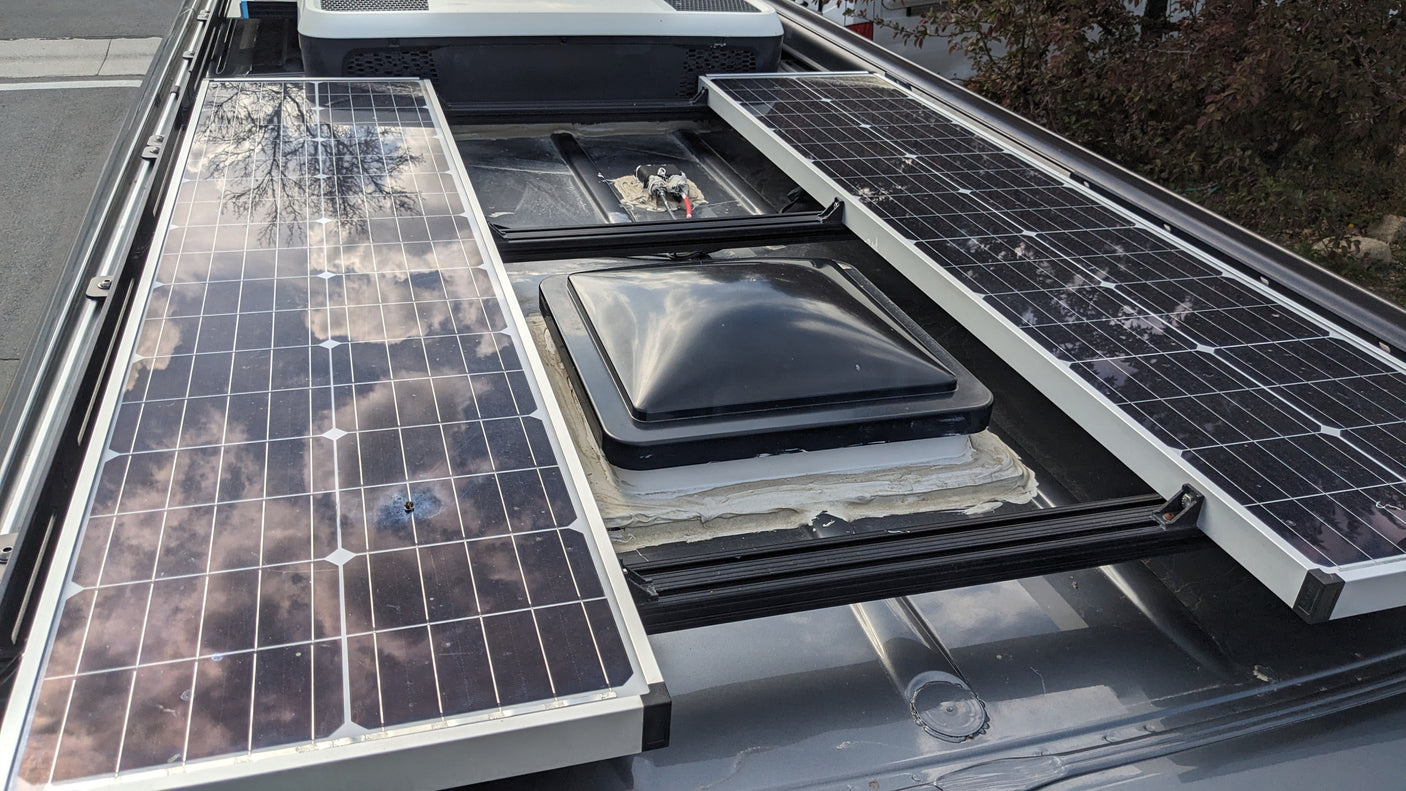 RV rental roof: two solar panels flank a black roof vent, an open compartment with wiring, and a large white AC unit.