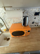 This inviting RV rental kitchen features an orange retro microwave, a sleek kettle, a practical sink, and a modern tiled backsplash.