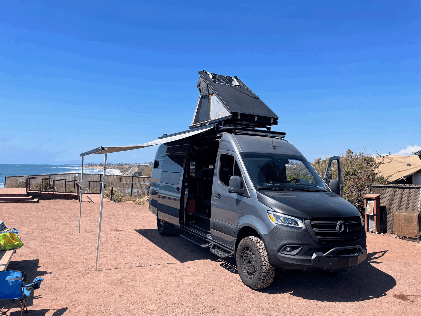 Custom RV rental: A Sprinter van with a rooftop tent and awning, perfectly set up for oceanfront camping.