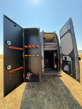 Inside this RV rental van: custom storage unit with orange racks, a comfy bed, perfect for gear & rest on the go.
