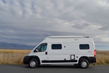 White Winnebago Solis RV rental parked by snowy mountains & fields under cloudy sky. Perfect for adventure!