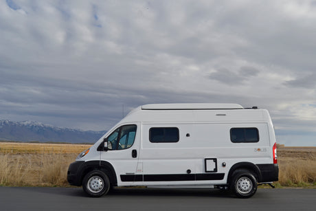 White Winnebago Solis RV rental parked by snowy mountains & fields under cloudy sky. Perfect for adventure!