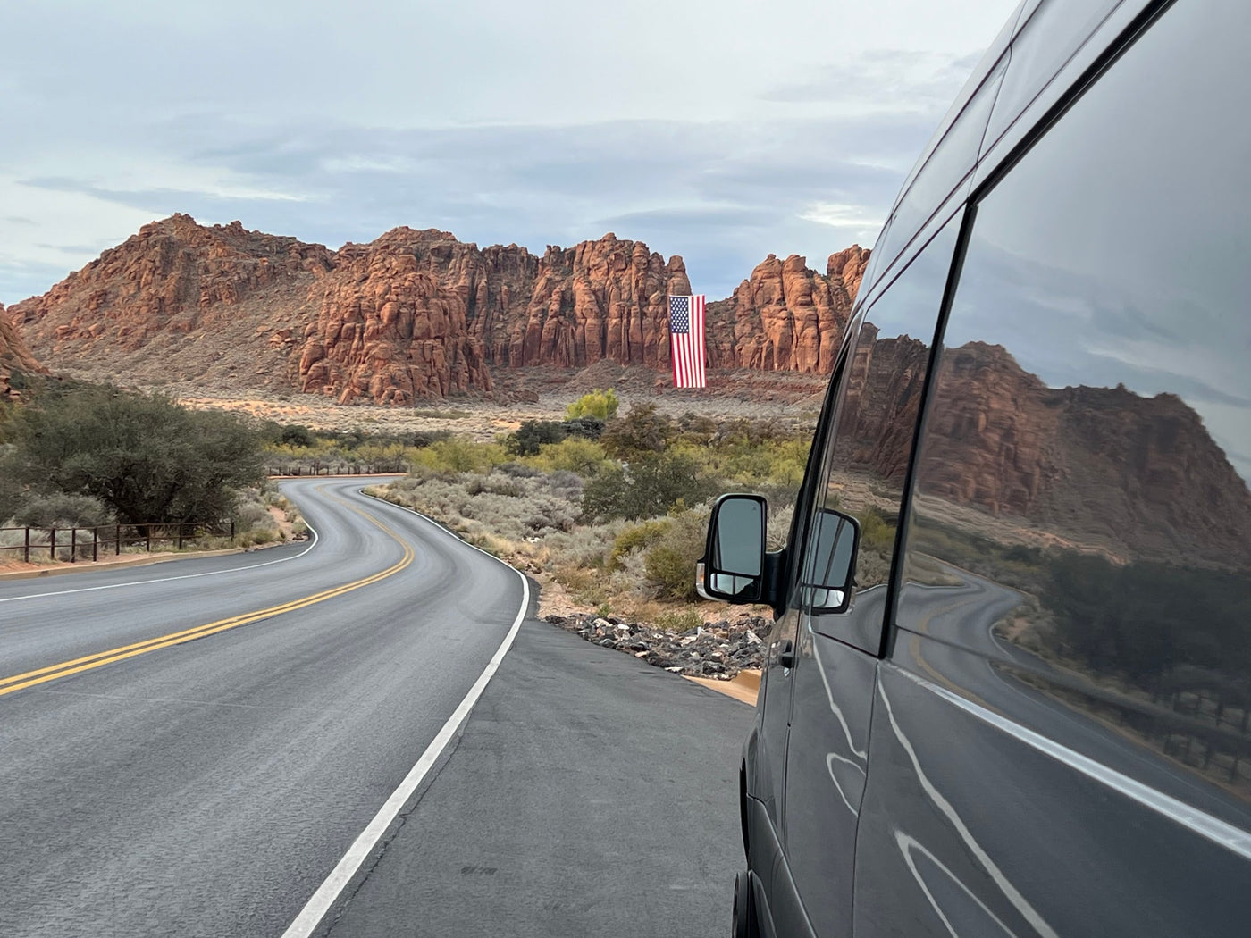 Enjoy a scenic rv rental road trip! Van parked by a winding desert road, with red rock mountains & a large US flag. — photo 7