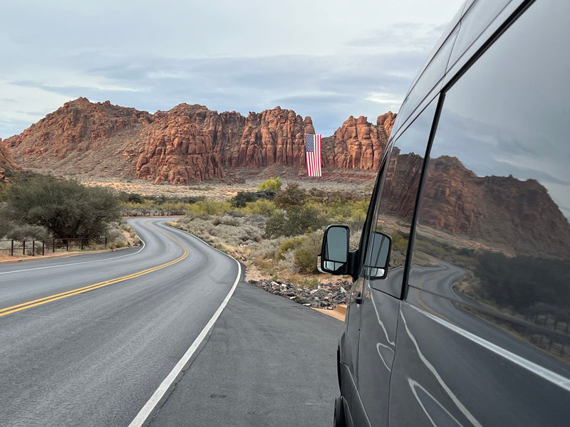 Enjoy a scenic rv rental road trip! Van parked by a winding desert road, with red rock mountains & a large US flag. — photo 7