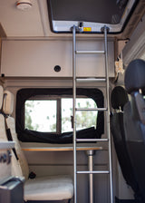 Interior of an RV rental: a ladder to an upper bunk, a table with a sink, and seating, ready for adventure.