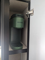 Compact green Keurig coffee maker on a shelf inside an RV rental cabinet, door open for access.