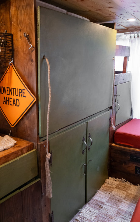 Explore our RV rental's cozy interior: olive green cabinets, wood walls, and an "ADVENTURE AHEAD" sign.