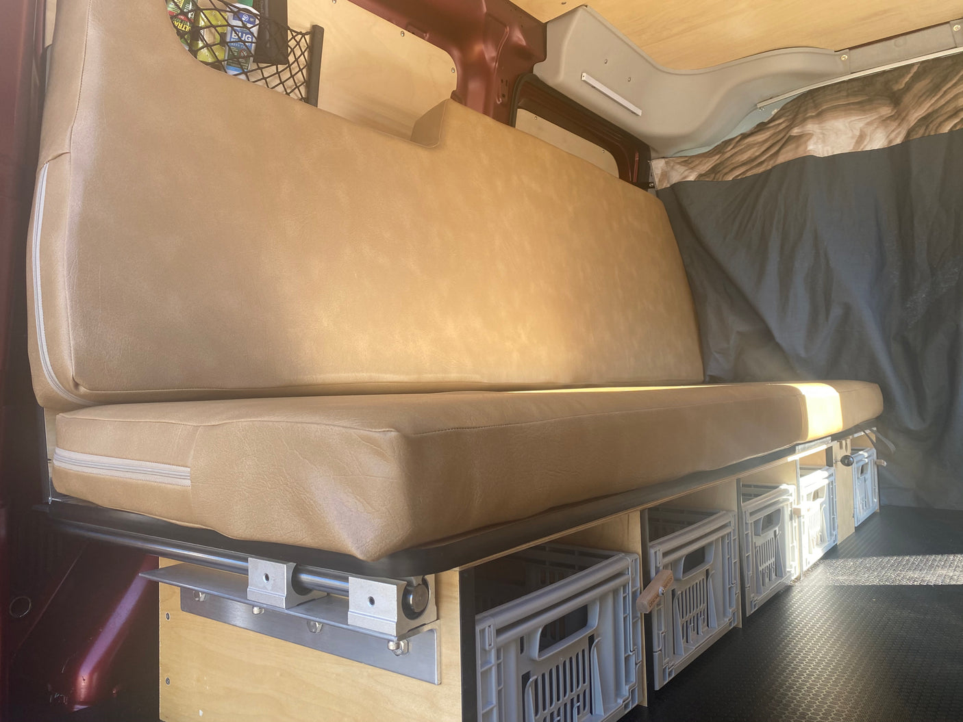 RV rental interior: comfy bench seat converts to a bed, with pull-out storage crates and wood-paneled walls.