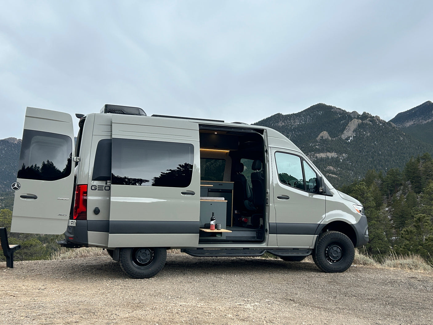 Adventure-ready Mercedes Sprinter camper van for rv rental, parked with open doors revealing interior and mountain views.