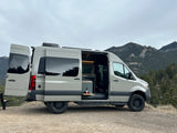 Adventure-ready Mercedes Sprinter camper van for rv rental, parked with open doors revealing interior and mountain views.