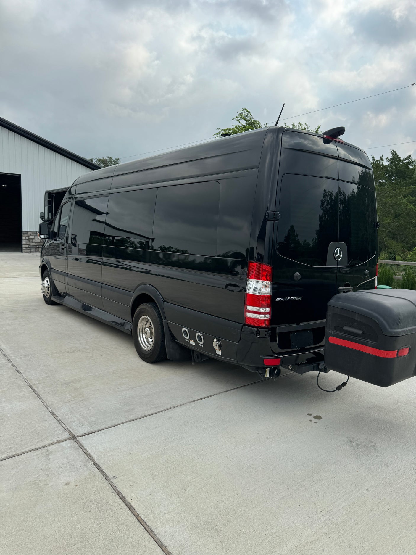Rear view of a black Mercedes-Benz Sprinter RV rental featuring dual rear wheels and a hitch-mounted storage box.