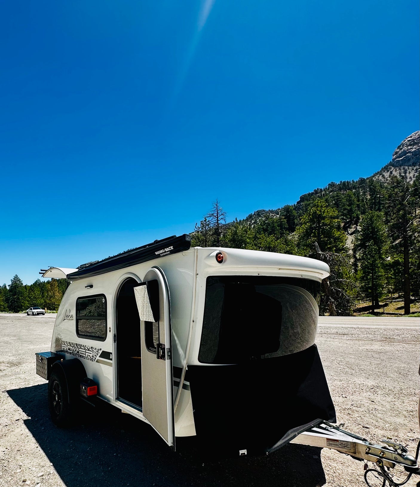 This Luna Rover teardrop RV rental is ready for adventure, parked in a scenic mountain area under a bright blue sky.
