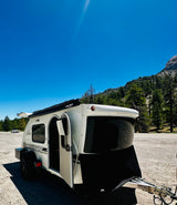 This Luna Rover teardrop RV rental is ready for adventure, parked in a scenic mountain area under a bright blue sky.