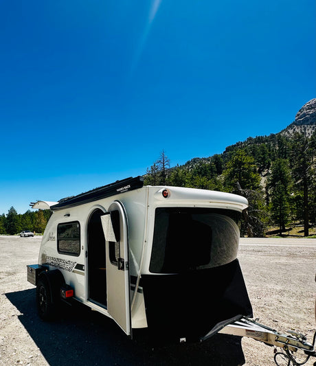 This Luna Rover teardrop RV rental is ready for adventure, parked in a scenic mountain area under a bright blue sky.