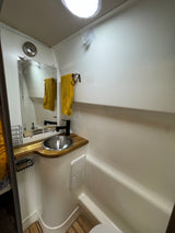 Modern RV rental bathroom features a small sink, mirror, black faucet, and yellow towel in a compact, white-walled space.
