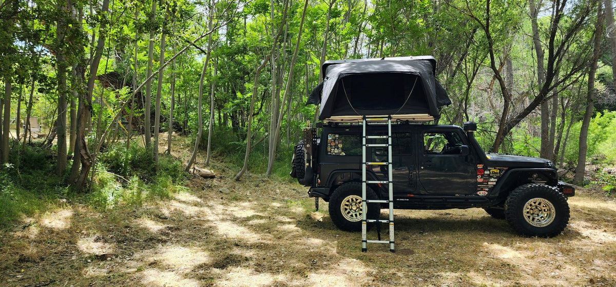 iKamper Skycamp 3.0 opened at a wooded campsite showing the fold-out floor extension and telescoping ladder — photo 2