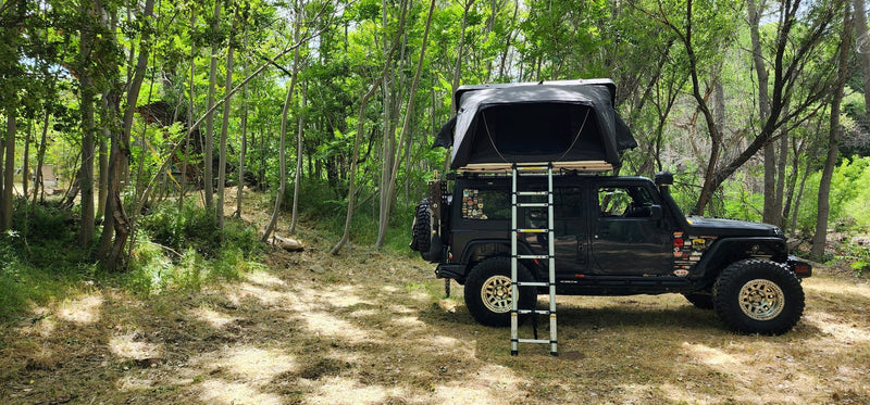 iKamper Skycamp 3.0 opened at a wooded campsite showing the fold-out floor extension and telescoping ladder — photo 2