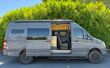 A gray customized Sprinter camper van with its side door open, revealing the interior; perfect for an RV rental adventure.