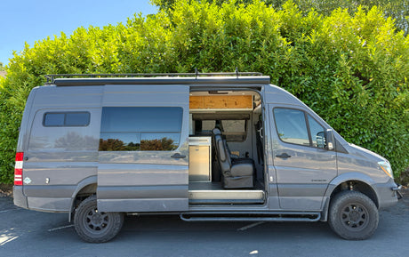A gray customized Sprinter camper van with its side door open, revealing the interior; perfect for an RV rental adventure.