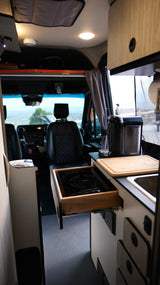 Inside a modern RV rental: kitchenette with induction cooktop, sink, Nespresso, and front cabin view of a scenic landscape.
