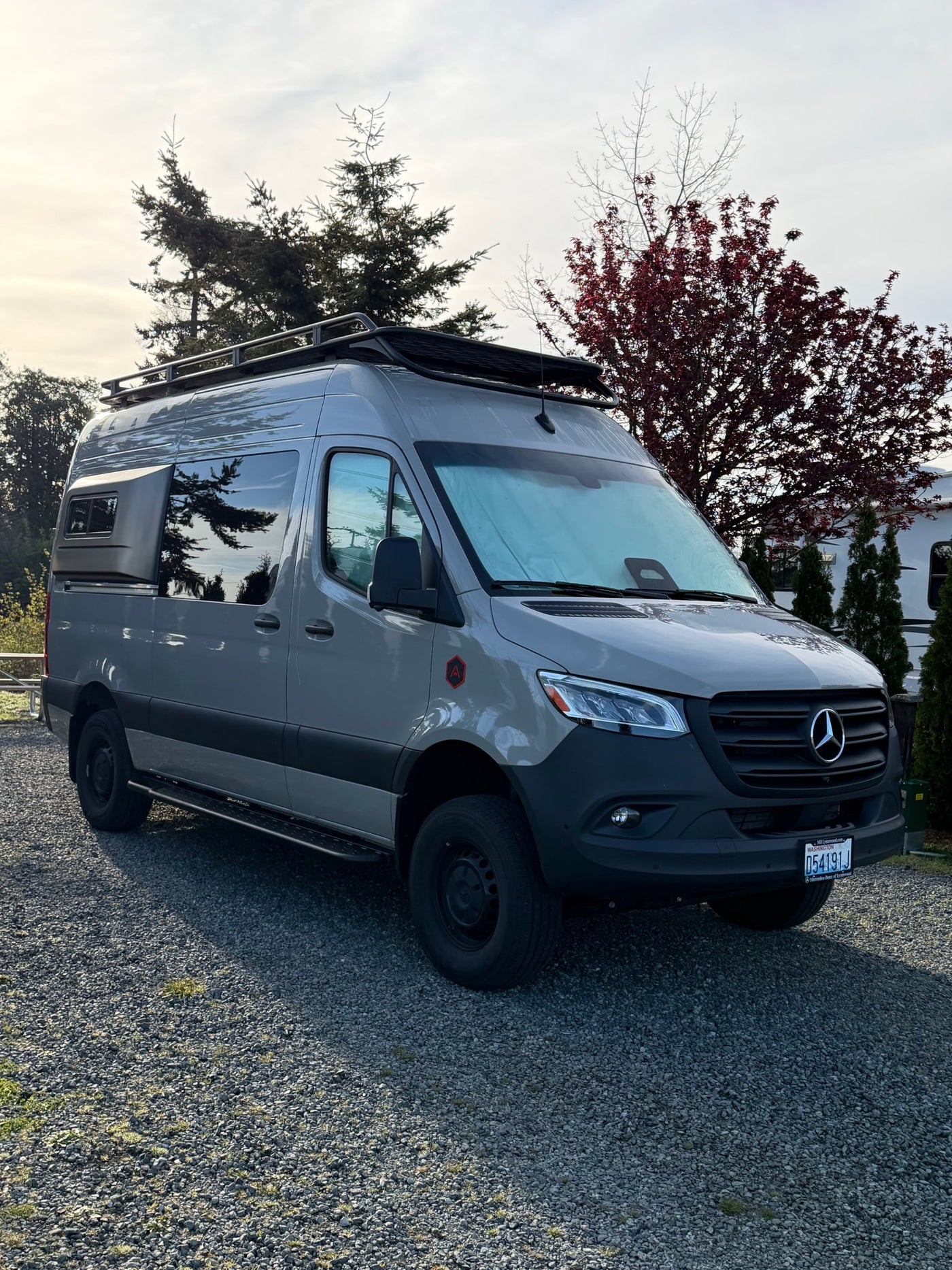 This custom gray Mercedes-Benz Sprinter camper van, ideal for RV rental, is parked on gravel among trees. — photo 12