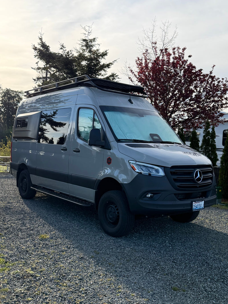 This custom gray Mercedes-Benz Sprinter camper van, ideal for RV rental, is parked on gravel among trees. — photo 12