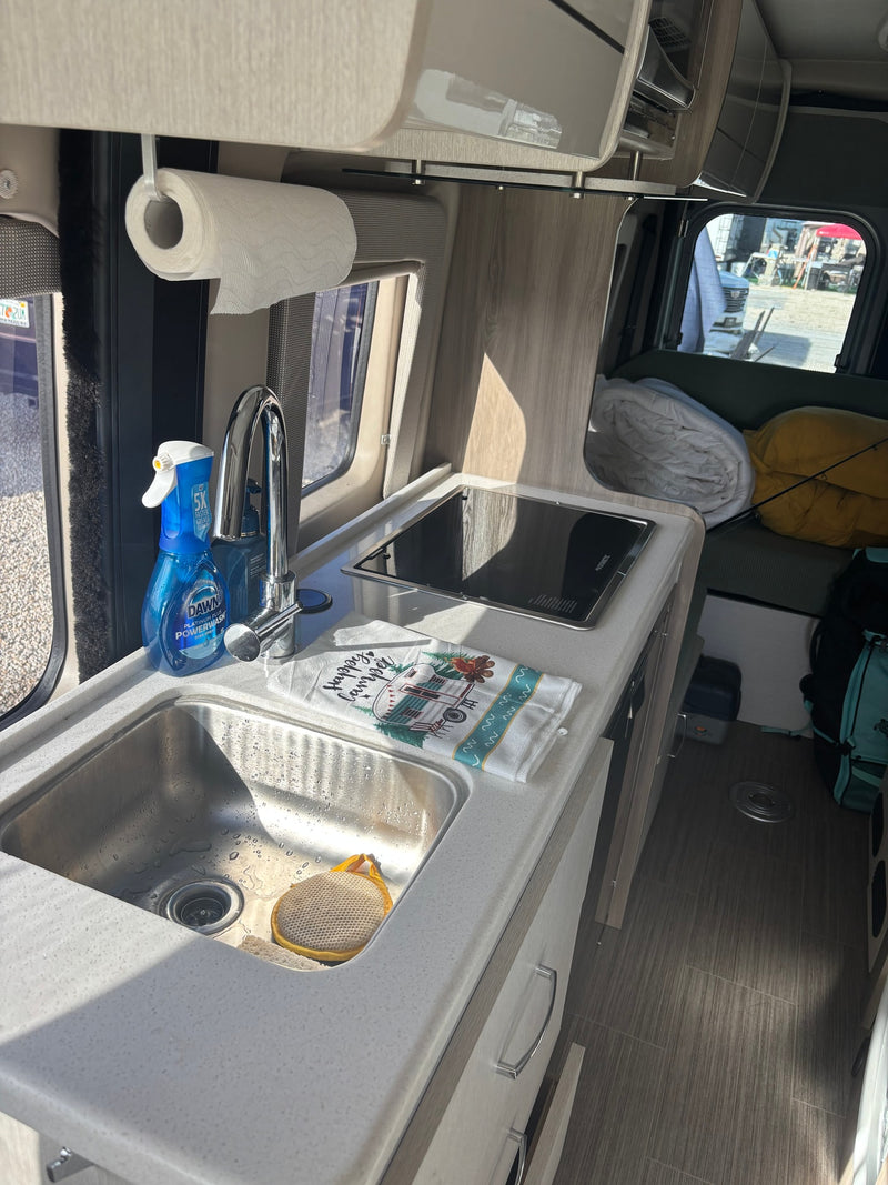 Compact RV rental kitchen features a sink, stove, Dawn Powerwash, and "Happy Camper" towel, ready for adventure. — photo 7