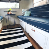 Bright RV rental interior: blue striped cushions, white storage, copper accents, and a striped rug create a cozy space.
