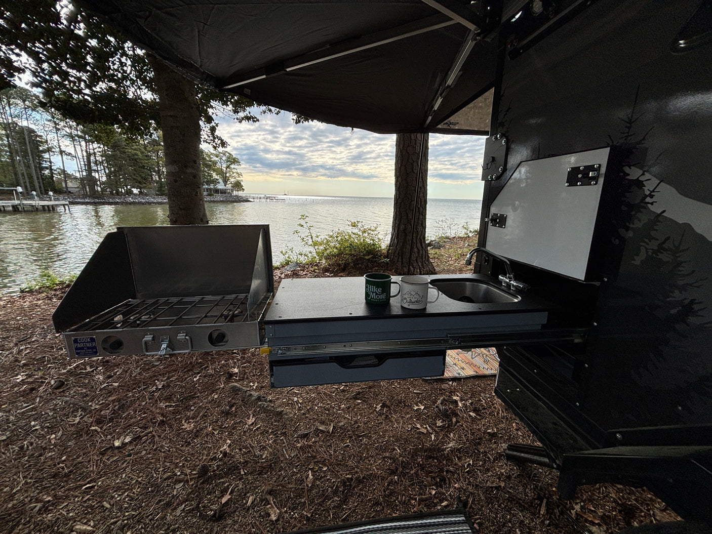 Enjoy lakeside camping with this RV rental's outdoor kitchen, featuring a stove, sink, and scenic water views.