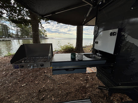 Enjoy lakeside camping with this RV rental's outdoor kitchen, featuring a stove, sink, and scenic water views.
