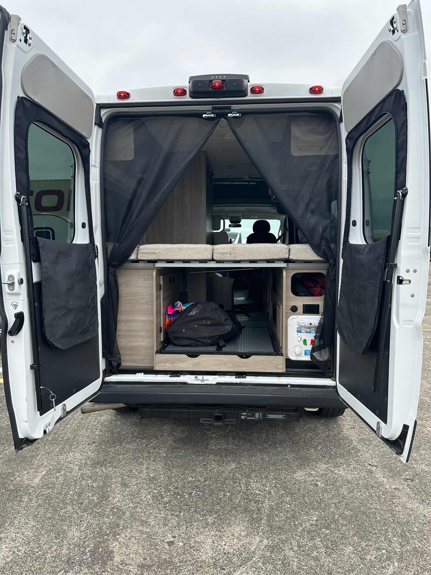 Open rear doors of an RV rental, revealing a bed, pull-out storage, and water utilities for easy access.