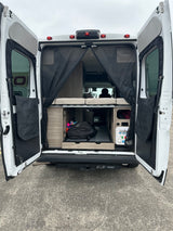 Open rear doors of an RV rental, revealing a bed, pull-out storage, and water utilities for easy access.