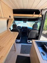 RV rental: View inside a custom camper van showing a wood kitchen, dining table, and front driver's cabin.