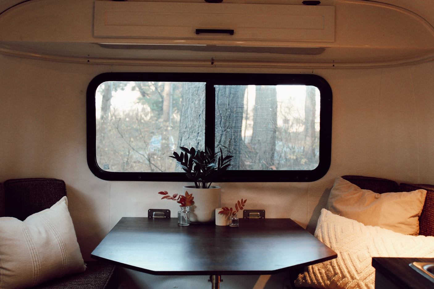 Inside a cozy RV rental: dinette with dark table, cushions, and a large window showcasing a natural view.