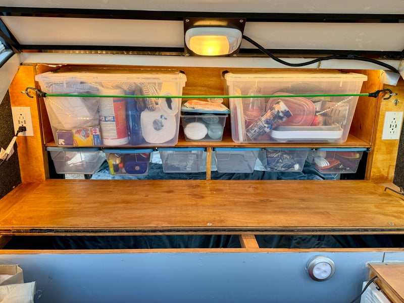Organized RV rental interior with clear bins, bungee cords, & power outlets. Efficient storage for camping essentials. — photo 13