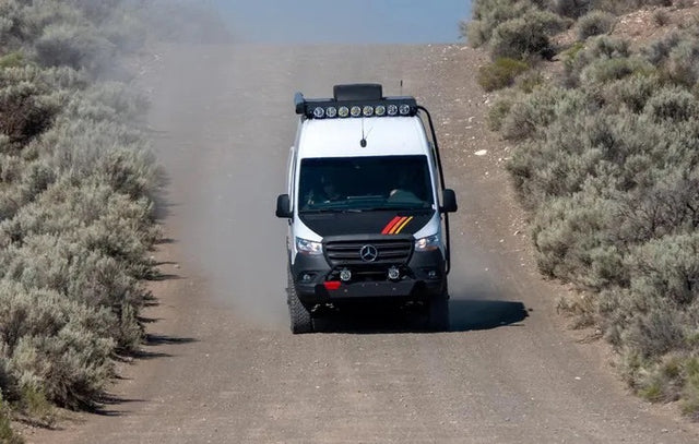 A rugged Mercedes Sprinter adventure van, an ideal RV rental, kicks up dust on a desert dirt road.