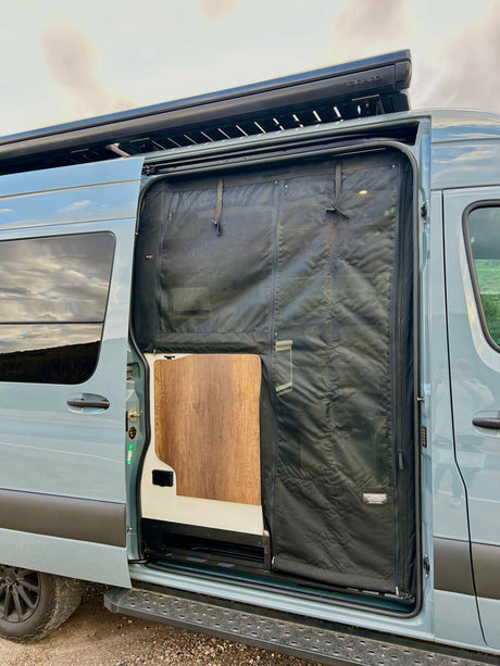 Open side of an RV rental camper van, showing a black ROLEF mesh screen, wood interior & GRARD awning.