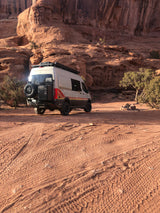 An RV rental camper van parked in a beautiful desert landscape with large red rock cliffs. Perfect for rugged off-grid camping adventures.