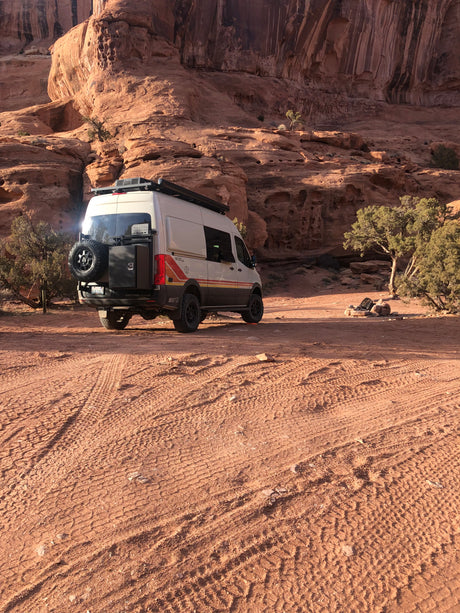 An RV rental camper van parked in a beautiful desert landscape with large red rock cliffs. Perfect for rugged off-grid camping adventures.