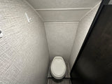 Compact RV rental bathroom interior featuring a white toilet, textured grey walls, and a convenient wall hook.