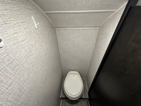 Compact RV rental bathroom interior featuring a white toilet, textured grey walls, and a convenient wall hook.