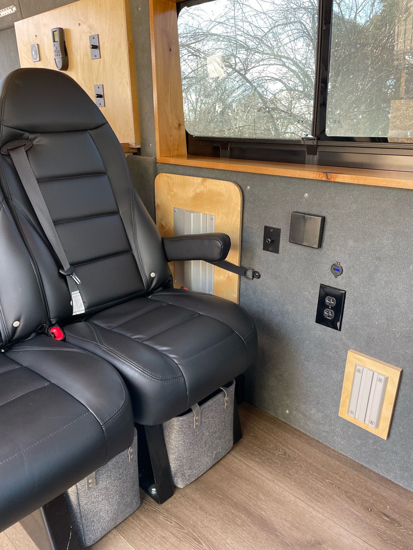 Inside a modern RV rental: ergonomic black leather seats, a large window, and integrated power/light controls.