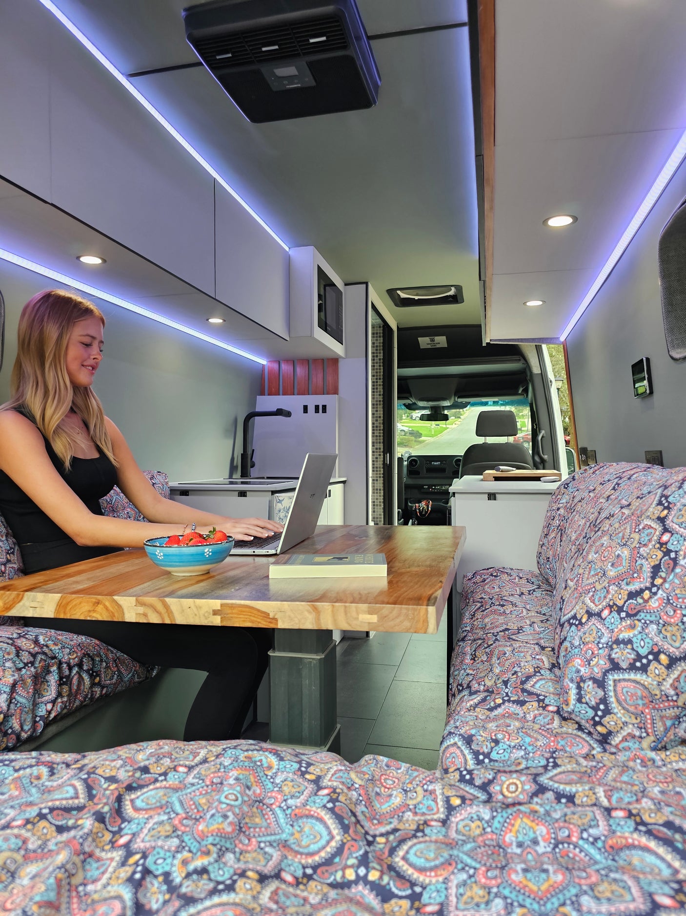 Productive day in a spacious campervan RV rental! Woman working on her laptop at a wooden table with fruit nearby.