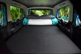 Cozy RV rental interior with a tropical view: bed, pillows, fans, and vibrant curtains ready for adventure.