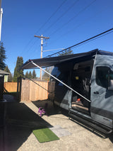 Gray RV rental camper van with extended awning, parked in a sunny yard. Ready for adventure!