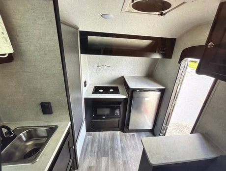 Functional RV rental kitchen: sink, two-burner stove, microwave, and refrigerator. Essential amenities for travel.