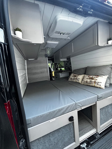 Modern grey & white rv rental campervan interior with bed, kitchenette, and overhead storage. Ready for your adventure.