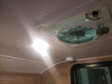 Overhead view in an RV rental: bright ceiling light, vent fan with controls, smoke detector, and window below.