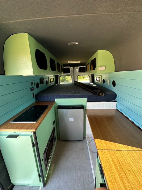 Modern RV rental interior, featuring a bright green and blue kitchen, sleeping area, and storage.
