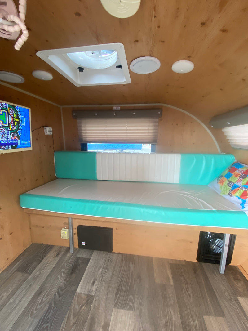 RV rental interior: light wood walls, teal & white bench seating, a ceiling fan, and TV on the left. — photo 9